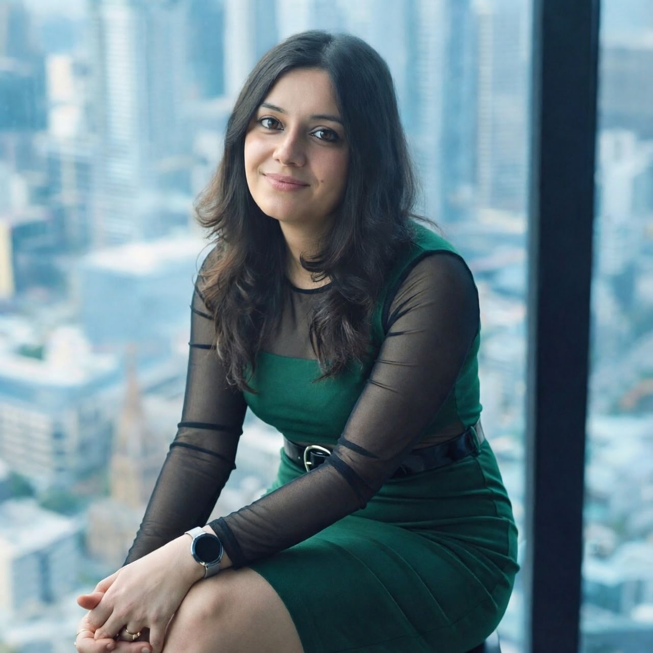 Woman in a green dress sitting by a window with a cityscape view