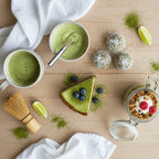 A bright and colorful flat-lay of various matcha-infused foods on a wooden table. Pictured are a few green matcha energy balls, a slice of matcha cheesecake, a glass jar of matcha overnight oats, and a small bowl of matcha-lime salad dressing. Appealing, modern food photography.