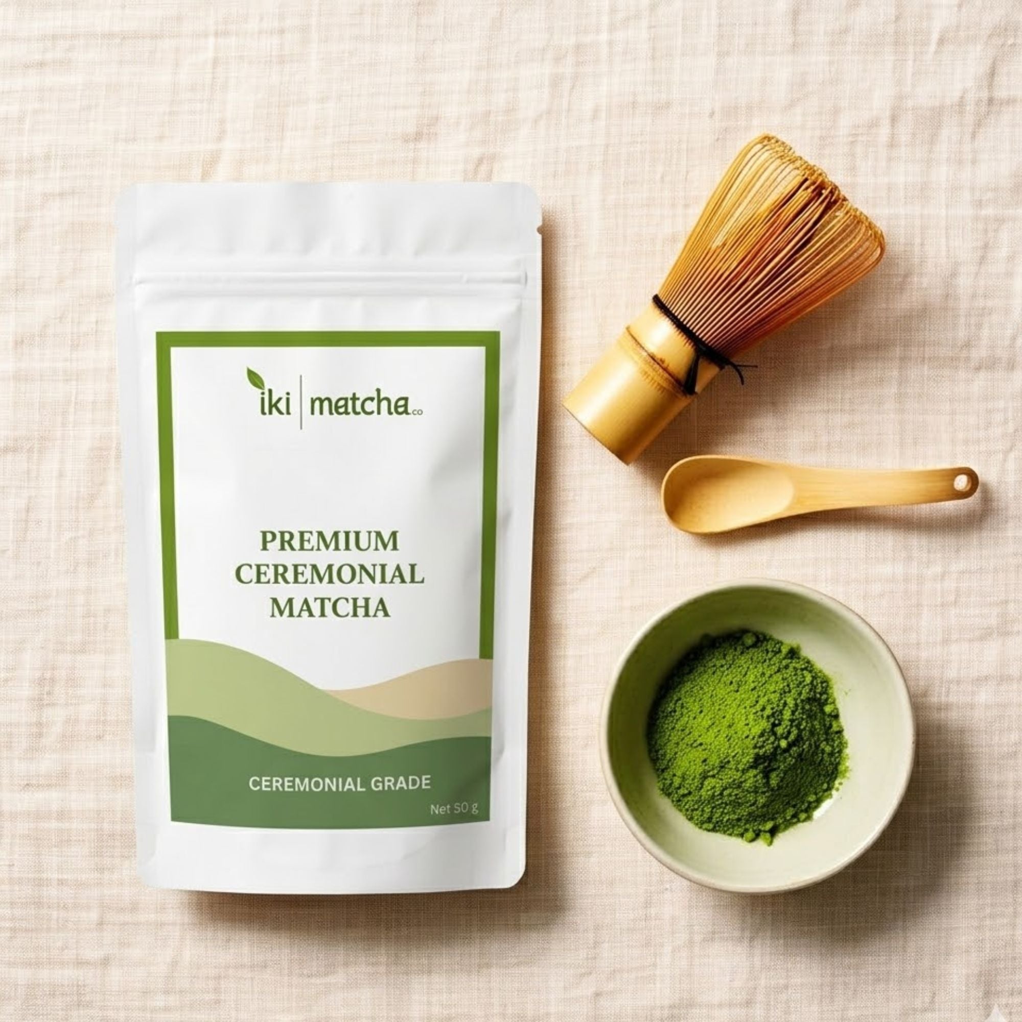 Packaging of iki matcha premium ceremonial matcha with a bowl of green powder and tea-making tools on a beige fabric background.